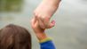 Vertrauen – Symbolfoto: kleines Kind hält Hand eines Erwachsenen; © dpa/Fernando Gutierrez-Juarez