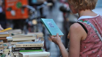 Menschen schauen sich in Berlin vor einem Geschäft an der Oranienstraße Bücher an. © picture alliance / dpa | Paul Zinken