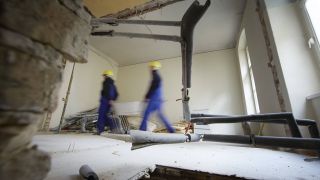 Zwei Bauarbeiter tragen eine Metallwanne bei der Sanierung eines Altbaus. © IMAGO / photothek / Thomas Koehler
